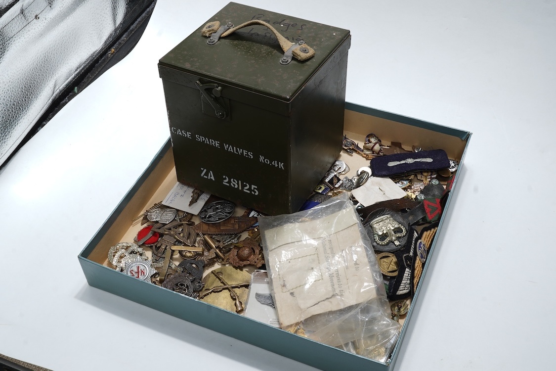 A collection of primarily 20th century military badges, lapel badges, shoulder titles, and other related ephemera, including seventeen military cap badges, cloth badges, ARP badges, etc., together with a military tin box